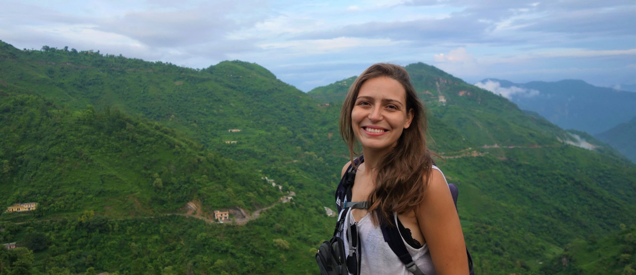 Girl smiles to the camera with woody hills behind